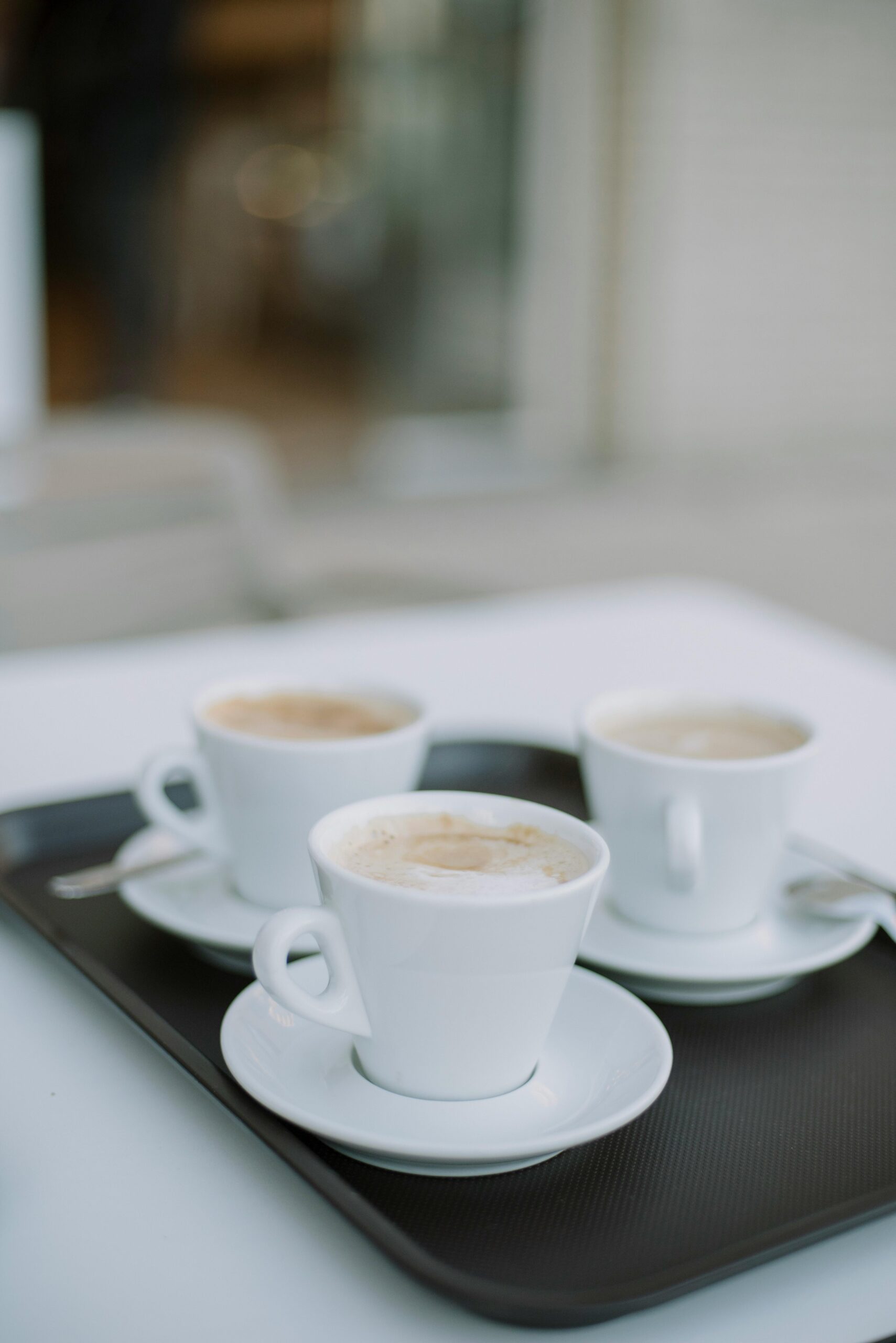 Three cappuccino cups with foam on a tray in an outdoor cafe.